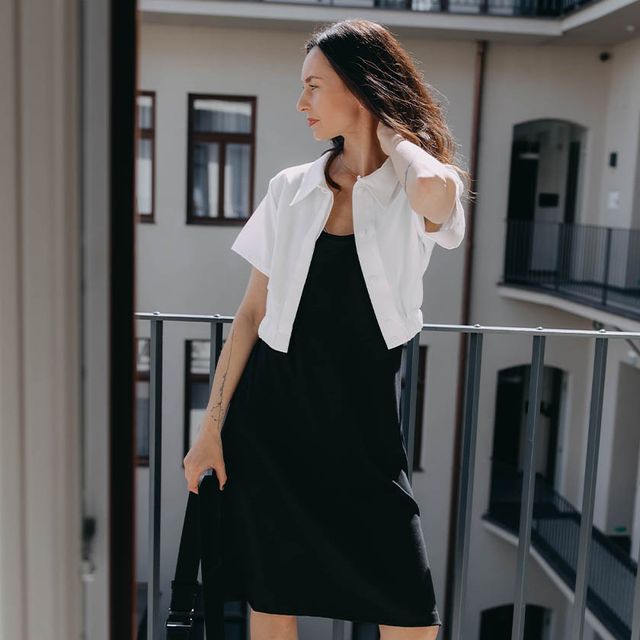 Minimalistické černé šaty nad kolena skvěle fungují s bílou crop košilí. Ivana si vybrala a oblékla právě tyto kousky z české kolekce od Bugy.