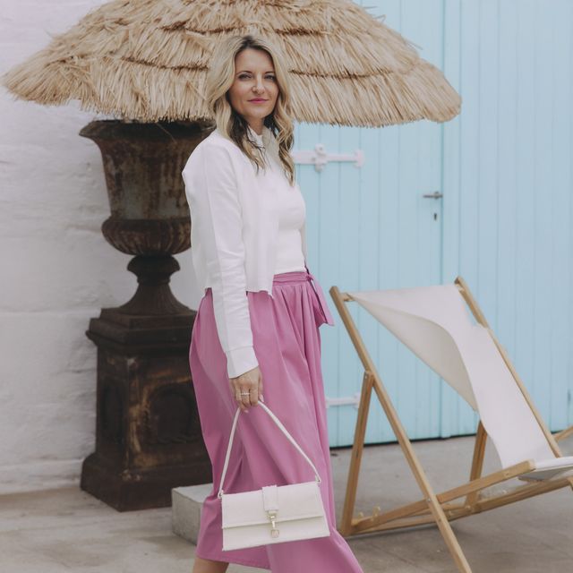 Káťa má na sobě krásný komplet vytvořený z bílé crop košile a růžové sukně do gumy, která má midi délku a pásek na ozdobu. Oboje z české kolekce Buga.